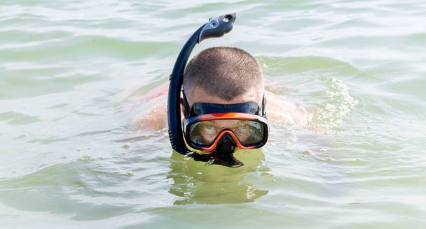Man met snorkeluitrusting: snorkel en duikmasker op het zeewater - Foto, afbeelding