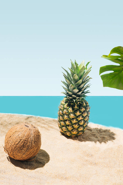 Un coco natural, piña orgánica y hoja de monstera en la playa de arena, concepto para las vacaciones de verano. - Foto, imagen
