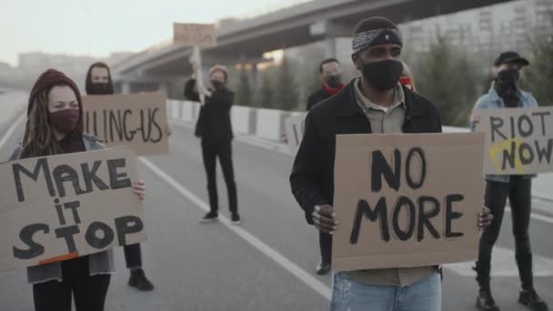 Handheld slow-mo tiro de jovens em máscaras faciais bloqueando estrada e protestando com sinais - Filmagem, Vídeo
