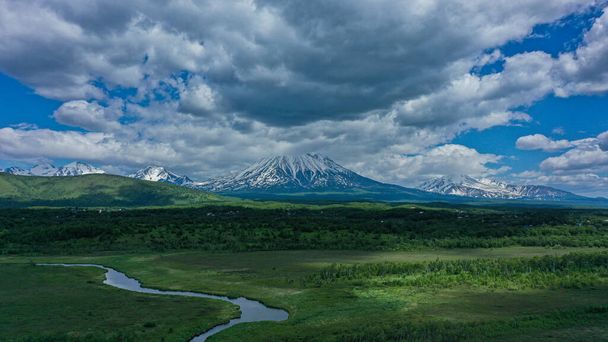 Paesaggio pittoresco con fiume e vulcano. Penisola di Kamchatka. Vulcano Koryakskiy sullo sfondo. Cielo blu con nuvole bianche tempestose. Kamchatka in giugno - Foto, immagini