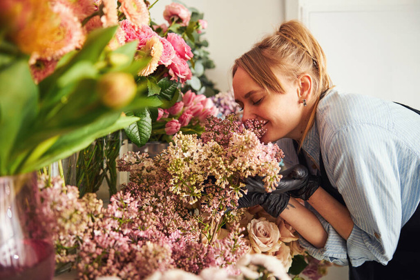 Улыбающаяся флористка с закрытыми глазами, пахнущая сиренью - Фото, изображение