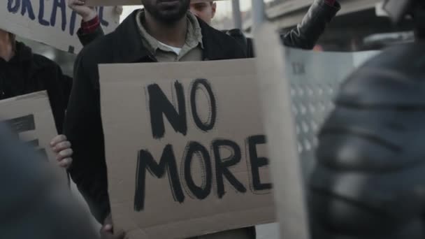 Медленный снимок неузнаваемой группы людей, держащих плакаты и протестующих перед офицерами ОМОНа со щитами - Кадры, видео