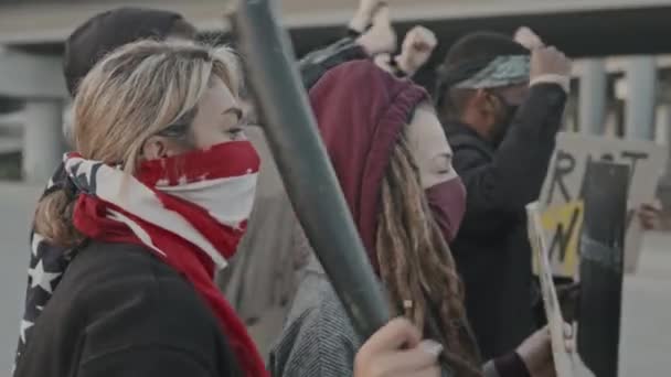 Slowmo nyomkövető felvétel maszkos fiatalokról, jelekkel kántálva és tiltakozva a megfélemlítő rohamrendőrtisztek csoportja előtt, pajzsokkal. - Felvétel, videó