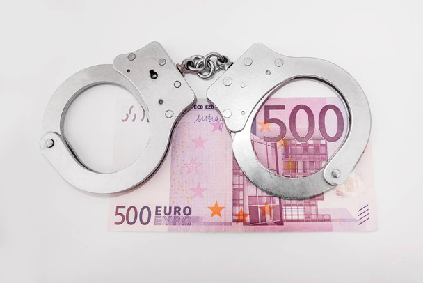 Dinheiro e algemas. O conceito de corrupção, fraude, lavagem de dinheiro. 500 euros e algemas cinza em um fundo branco. - Foto, Imagem