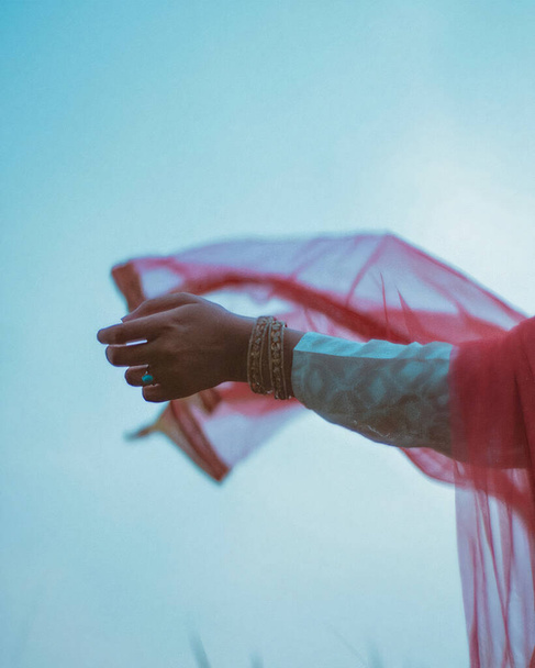 A vertical closeup shot of a soft female hand letting her red scarf move in the wind against blue sky - Foto, Imagem