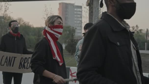 Slowmo tracking shot των μασκοφόρων νέων κρατώντας πινακίδες και ρόπαλο του μπέιζμπολ σε διαμαρτυρία - Πλάνα, βίντεο