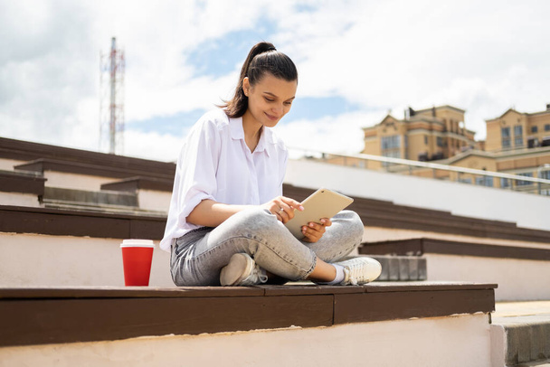 Счастливые молодые женщины держат планшет с чашкой кофе бумагу наслаждаясь солнечным днем сидя в городе - Фото, изображение
