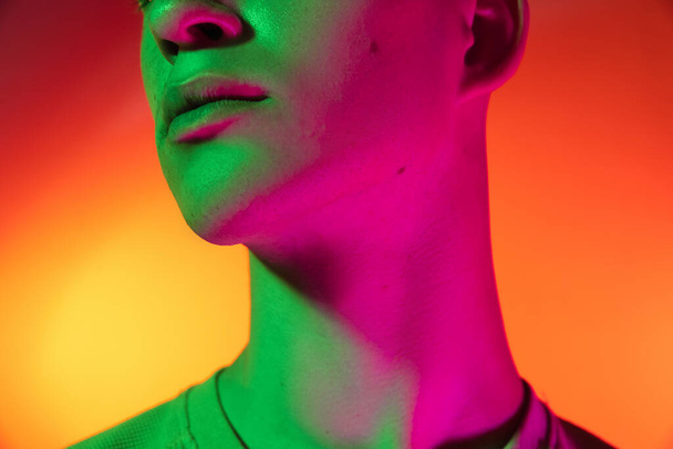 Cropped image of Caucasian young man isolated on orange studio background in neon light. Concept of human emotions, facial expression. - Photo, Image