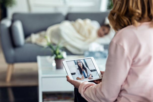 Shot of mature mother making videocall with young female doctor while caring for her sick daughter in living room at home. - Φωτογραφία, εικόνα