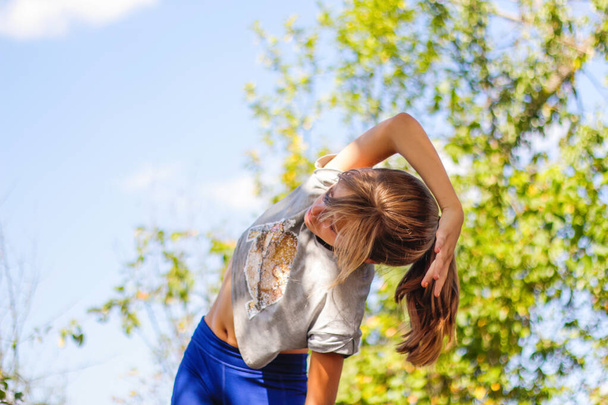 Дефокус кавказская девочка-подросток делает физические упражнения в парке, лесу, на открытом воздухе, на улице. Медитация, концентрация. Здоровый образ жизни. Упражнения на боковой изгиб. Природа. Не в фокусе - Фото, изображение