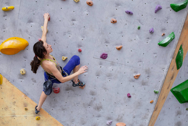 Glimlachend meisje klimt de klimwand op, de vrouw is bezig met extreme sporten, rotsklimmen in de stad, kracht- en uithoudingstraining - Foto, afbeelding