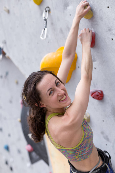 Smiling girl climbs the climbing wall, the woman is engaged in extreme sports, rock climbing in the city, strength and endurance training - Photo, Image