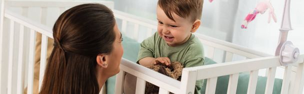 Usmívající se dítě s měkkou hračkou při pohledu na matku v ložnici, banner  - Fotografie, Obrázek