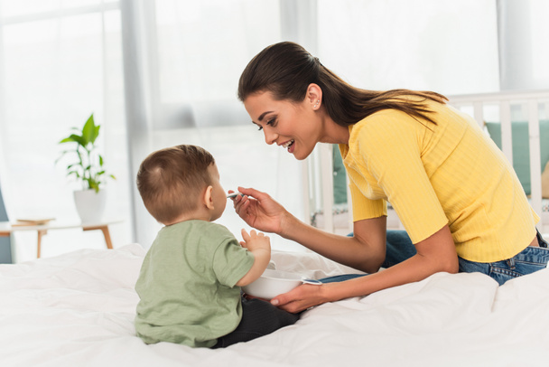 Cheerful mother feeding son on bed  - Photo, Image