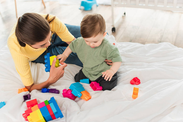 High angle view of mother and son playing building blocks on bedding  - Fotoğraf, Görsel