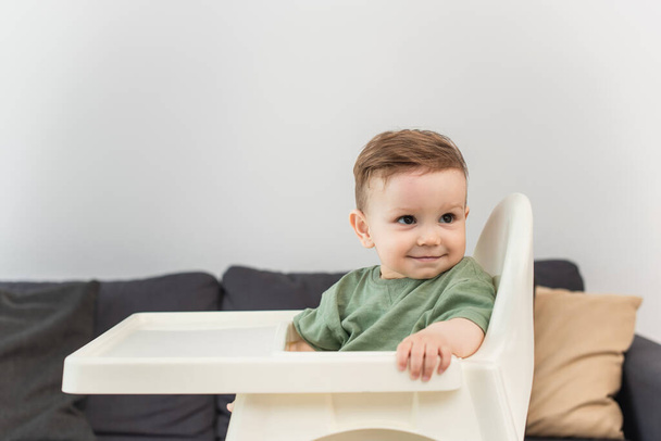 Smiling toddler boy looking away on high chair at home  - Fotó, kép