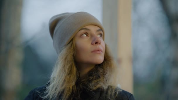 Женщина в зимней шляпе в холодный осенний день, смотрит вокруг задумчиво и печально - Кадры, видео