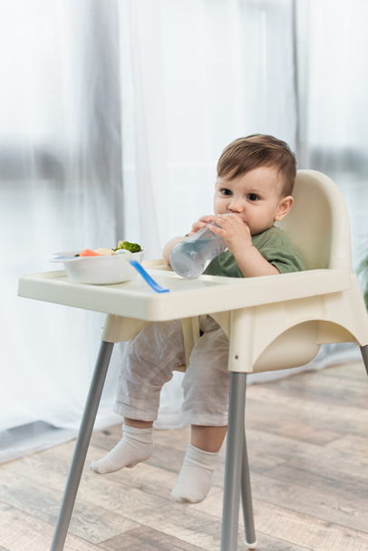 Child drinking water near vegetables in bowl on high chair  - Фото, зображення