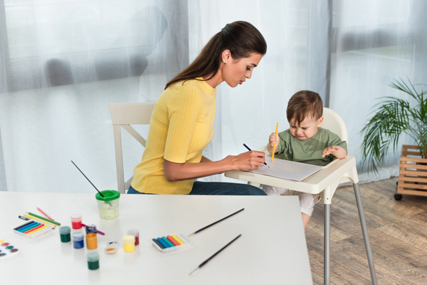 Dibujo de mujer con hijo en silla alta en casa  - Foto, Imagen