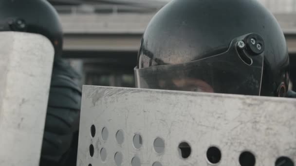 Close up slowmo shot of unrecognizable riot police officer in mask and helmet holding shield and standing in formation at protest - Footage, Video