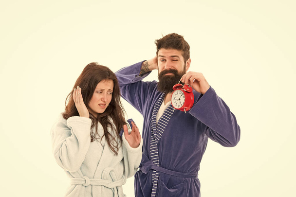A sleepy morning. Couple in love waking up in morning. Pretty woman and bearded man holding alarm clock early in the morning. Sexy girlfriend and brutal hipster wearing nightrobes in morning - Zdjęcie, obraz