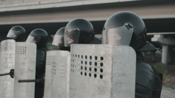Langzame tracking shot van onherkenbare oproerpolitie agenten in beschermende uitrusting slaan schilden met stokken en lopen in formatie - Video