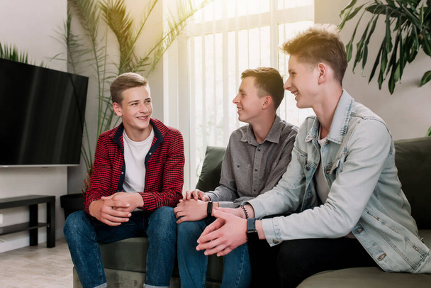 Трое друзей-мужчин разговаривают на зеленом диване в гостиной. Парни разговаривают, делятся и обсуждают новости, подбадривают друг друга. Сплетни о подростках - Фото, изображение