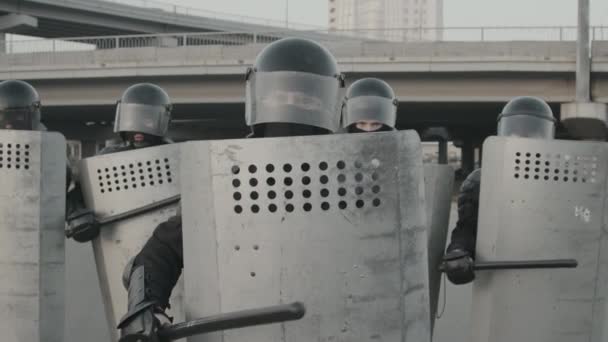 Медленная съемка офицеров ОМОНа в шестеренках, блокирующих улицу и бьющих дубинками по щитам при взгляде в камеру - Кадры, видео