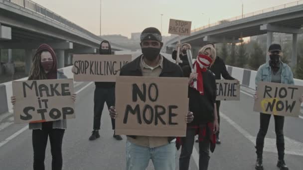 Slowmo dolly-out shot di gruppo di giovani mascherati con cartelli che bloccano la strada per protesta - Filmati, video