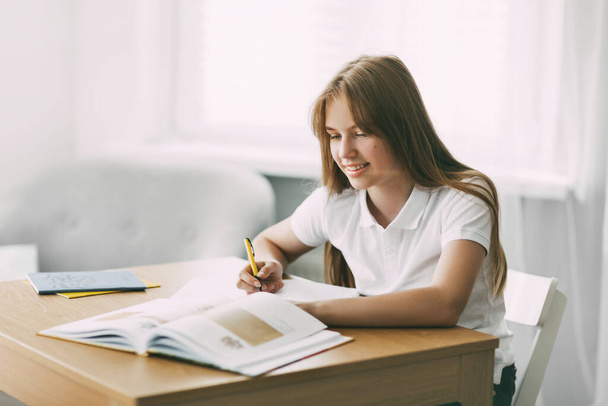 A high school student takes notes from a book, a teenage girl does her homework and prepares for lessons. Education, training, homework - Photo, Image