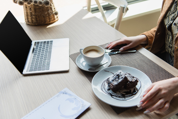 Vágott kilátás nő közelében ül kávé, sütemény és laptop üres képernyő kávézóban - Fotó, kép