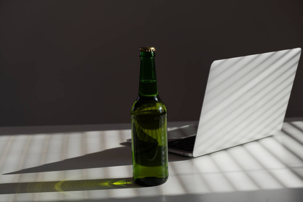 Beer bottle and laptop on white table. - Foto, Imagem