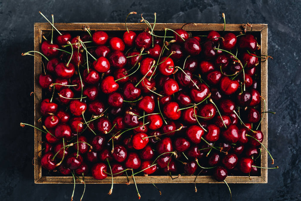 Cherry. Sweet Cherries in wooden box or crate on dark stone concrete background. Ripe Sweet Red Cherries. Top view. - Photo, Image