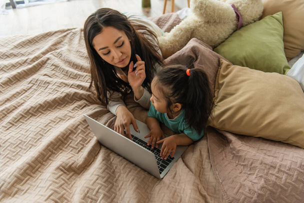 Overhead-Ansicht von asiatischen Mutter und Kind mit Laptop auf dem Bett  - Foto, Bild