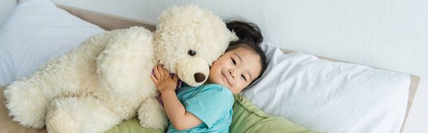 Asiatisches Kind liegt mit Teddybär auf Bett, Banner  - Foto, Bild