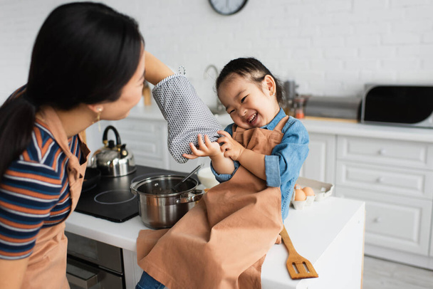 Blurred mother playing with asian daughter in kitchen  - Фото, изображение