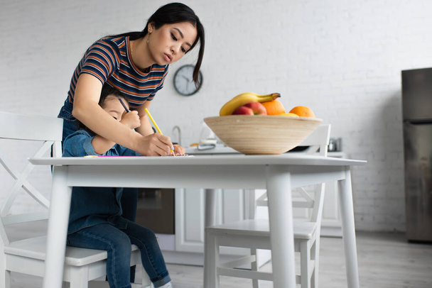 Asian woman drawing near daughter and blurred fruits  - Fotografie, Obrázek