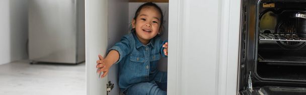 Cheerful asian kid sitting in kitchen cabinet, banner  - Foto, immagini