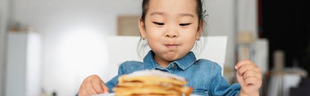 Asian toddler girl looking at blurred pancakes, banner  - Foto, imagen