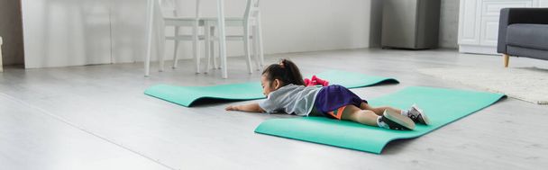 Маленькая азиатка в спортивной одежде лежит на коврике дома, баннер  - Фото, изображение