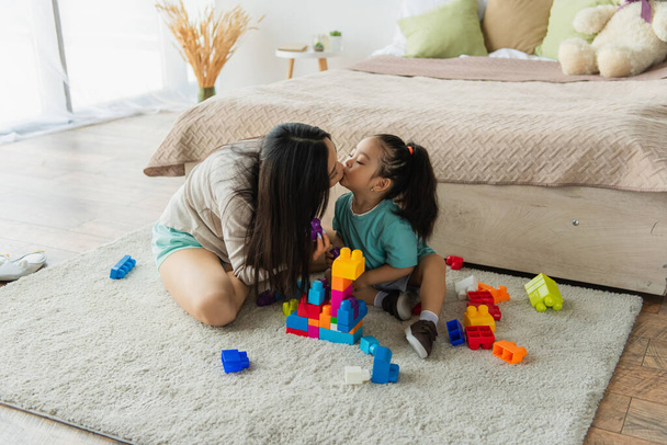 Asian mother and daughter kissing near building blocks at home  - 写真・画像