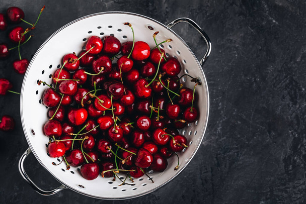 Cherry. Sweet Cherries in white colander on dark stone concrete background. Ripe Sweet Red Cherries. Top view, copy space - Photo, Image