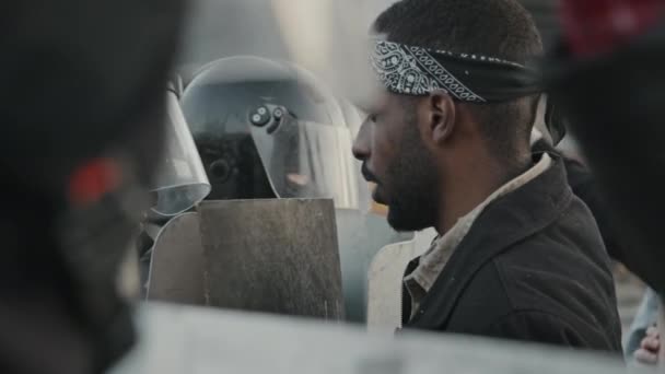 Langzame handheld schot van de jonge Afro-Amerikaanse man in hoofdband staan voor oproerpolitie agenten met schilden en schreeuwen bij protest - Video