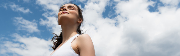nízký úhel pohledu na mladou šťastnou ženu v koruně obilí proti modré obloze s mraky, prapor - Fotografie, Obrázek