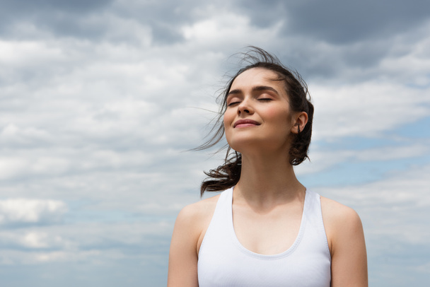 young pleased woman in crop top against blue sky with clouds  - Φωτογραφία, εικόνα