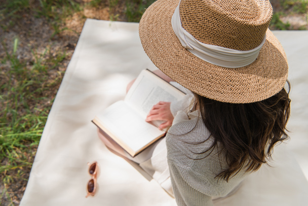 森の中で本を読む藁帽子の若い女性のオーバーヘッドビュー  - 写真・画像