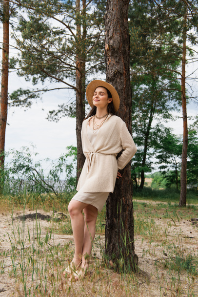 full length of smiling young woman in straw hat standing in forest - Fotografie, Obrázek