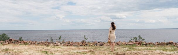 piena lunghezza di bruna giovane donna che tiene il cappello da sole e in piedi vicino al mare, banner - Foto, immagini