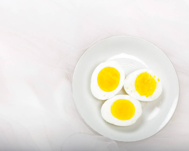 Fette d'uovo disposte su un piatto bianco. l'uovo viene tagliato proprio al centro del cerchio. Le uova di pollo cotte sono pronte da mangiare. Colore corrispondente Uova su uno sfondo luminoso. Uova sode. Sfocatura messa a fuoco - Foto, immagini