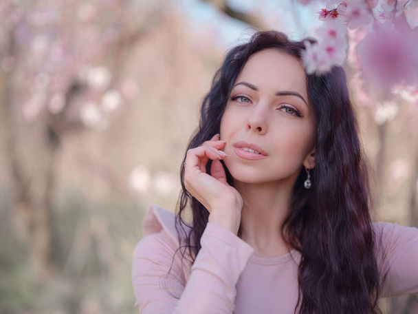 A beautiful young woman near a blooming spring cherry blossom tree. A celebration of spring and blossom like in Japan - Photo, Image
